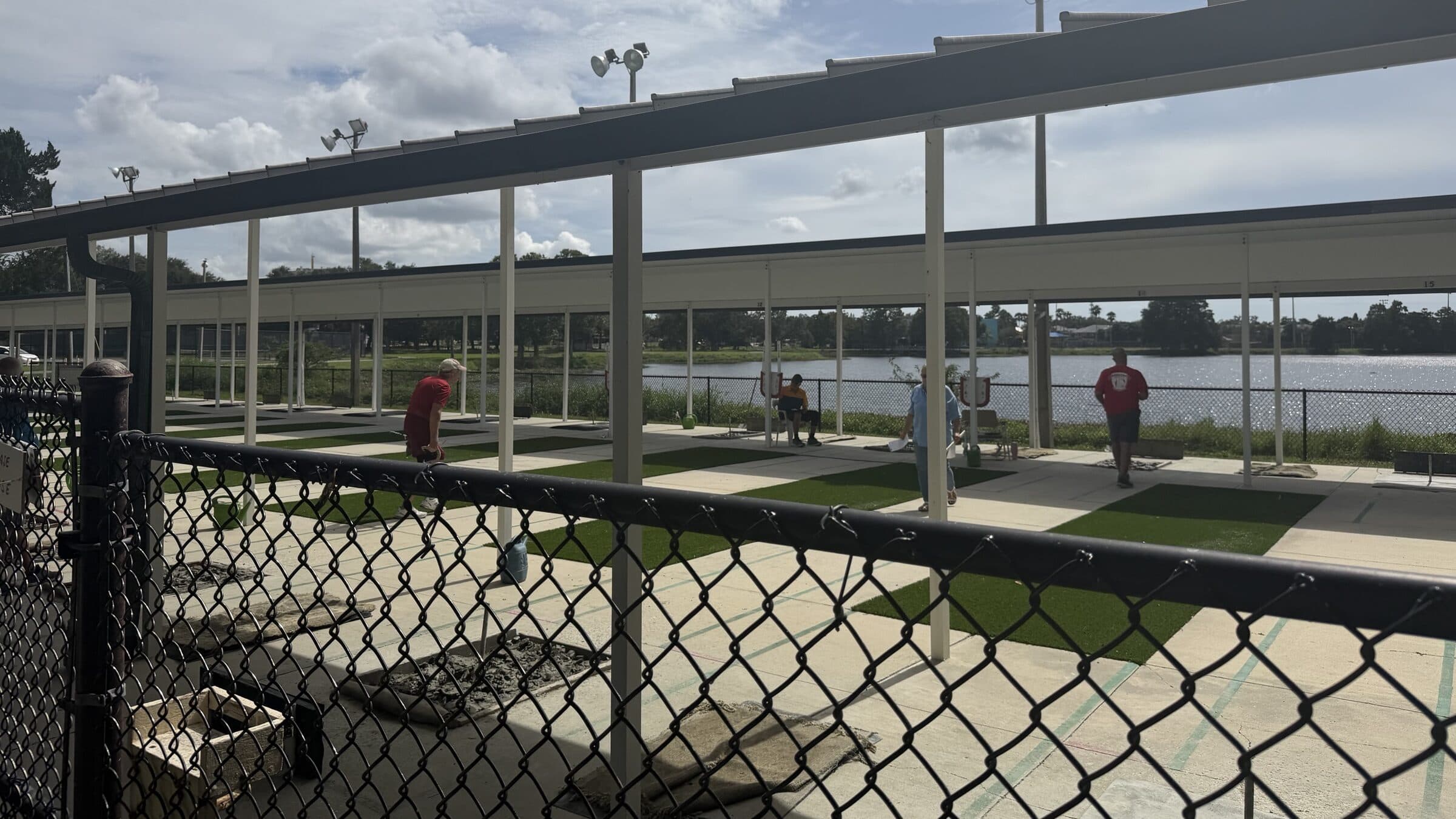 Members pitching and keeping score on the courts, seen through the fence, with the lake beyond