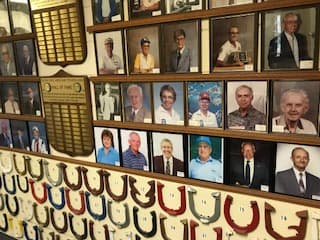 A closer view of Hall of Fame inductee portraits and plaques mounted above a row of championship horseshoes