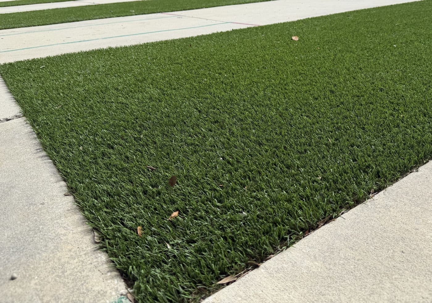 Close-up of the new Astroturf, trimmed flush against the concrete walkway beside a pit