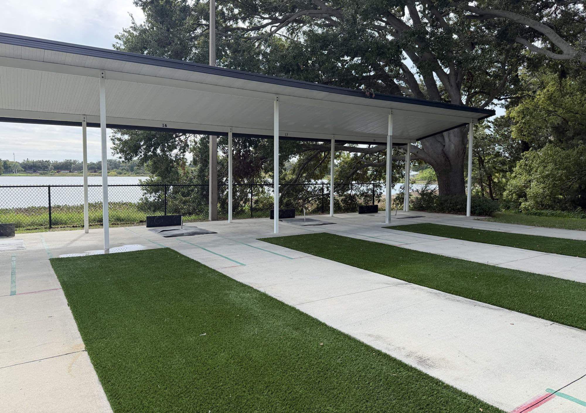 New Astroturf strips running between the pits at courts 16 through 18, under the covered roof with the lake and a live oak behind